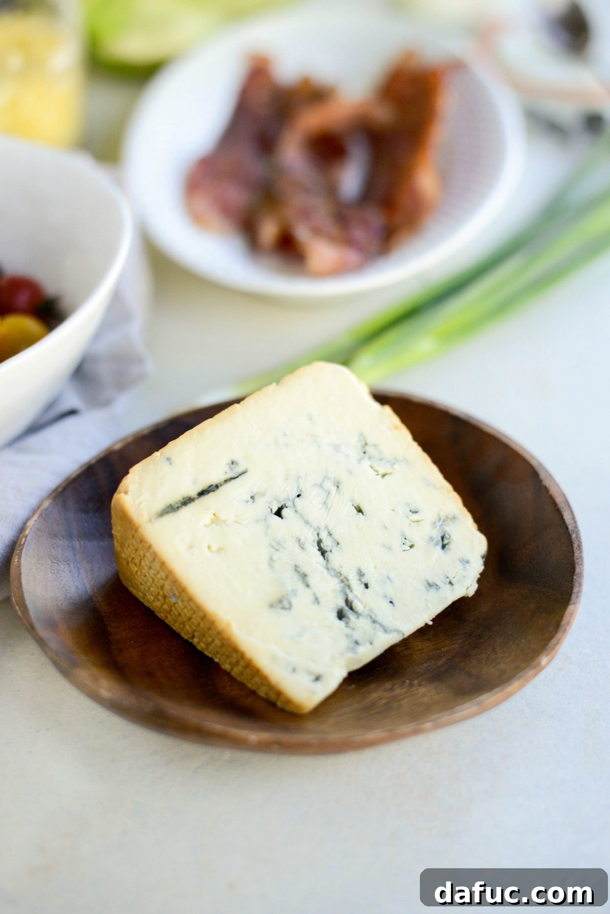Our Signature Loaded Wedge, Drenched in Peppercorn Buttermilk 7 Crumbled blue cheese in a small dish, showing its distinctive texture and color, ready for the salad.