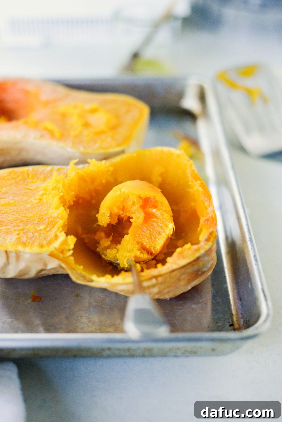 Scooping out the soft, roasted butternut squash flesh from its skin with a spoon.