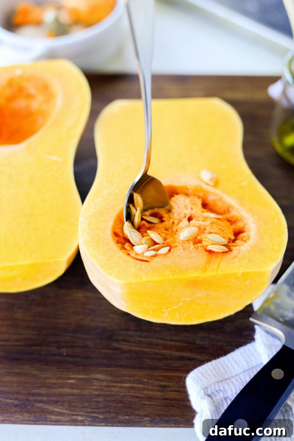 Using a spoon to scoop out and discard the seeds and fibrous strands from a halved butternut squash.