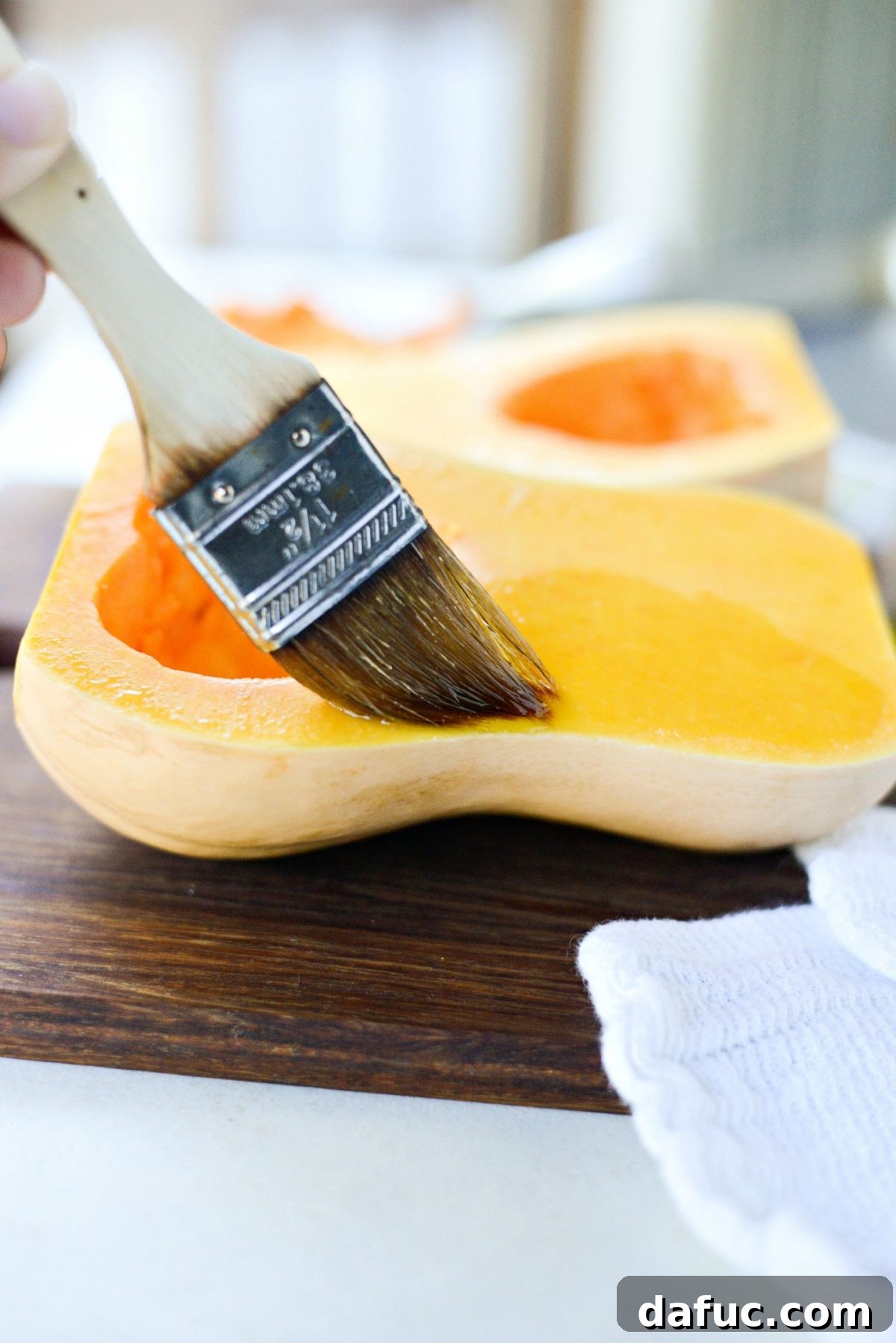 Brushing the cut side of a butternut squash half with light olive oil before roasting.