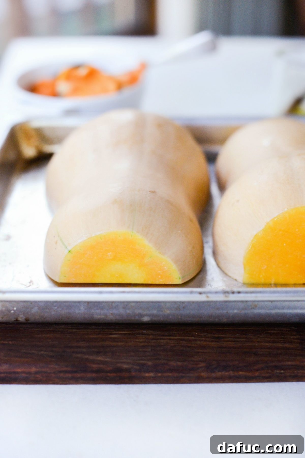 Butternut squash halves placed cut-side down on a rimmed baking sheet, ready for roasting.