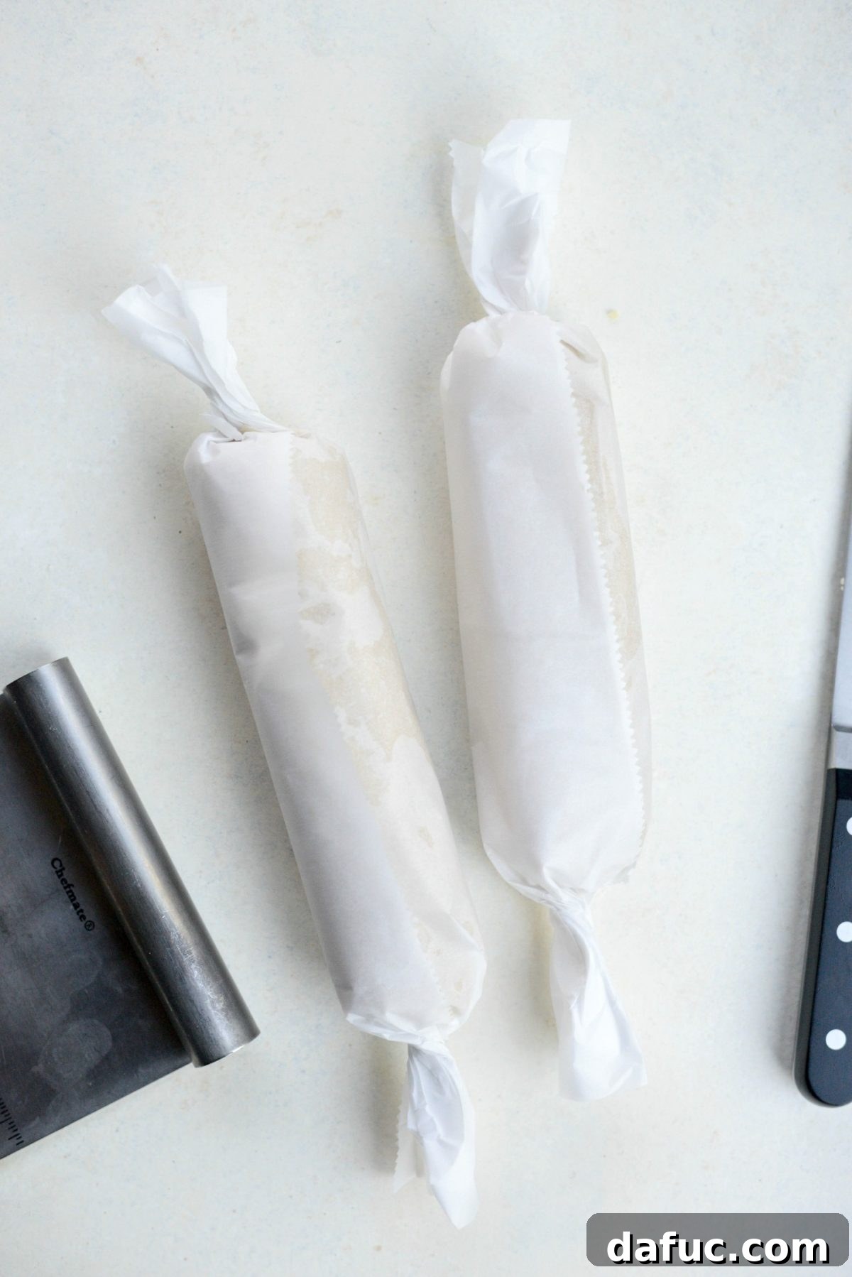 Form each dough half into logs, wrap in parchment paper, and chill - The two halves of Tahini Shortbread cookie dough are neatly shaped into logs and individually wrapped tightly in parchment paper, signifying they are prepared for the essential chilling step.