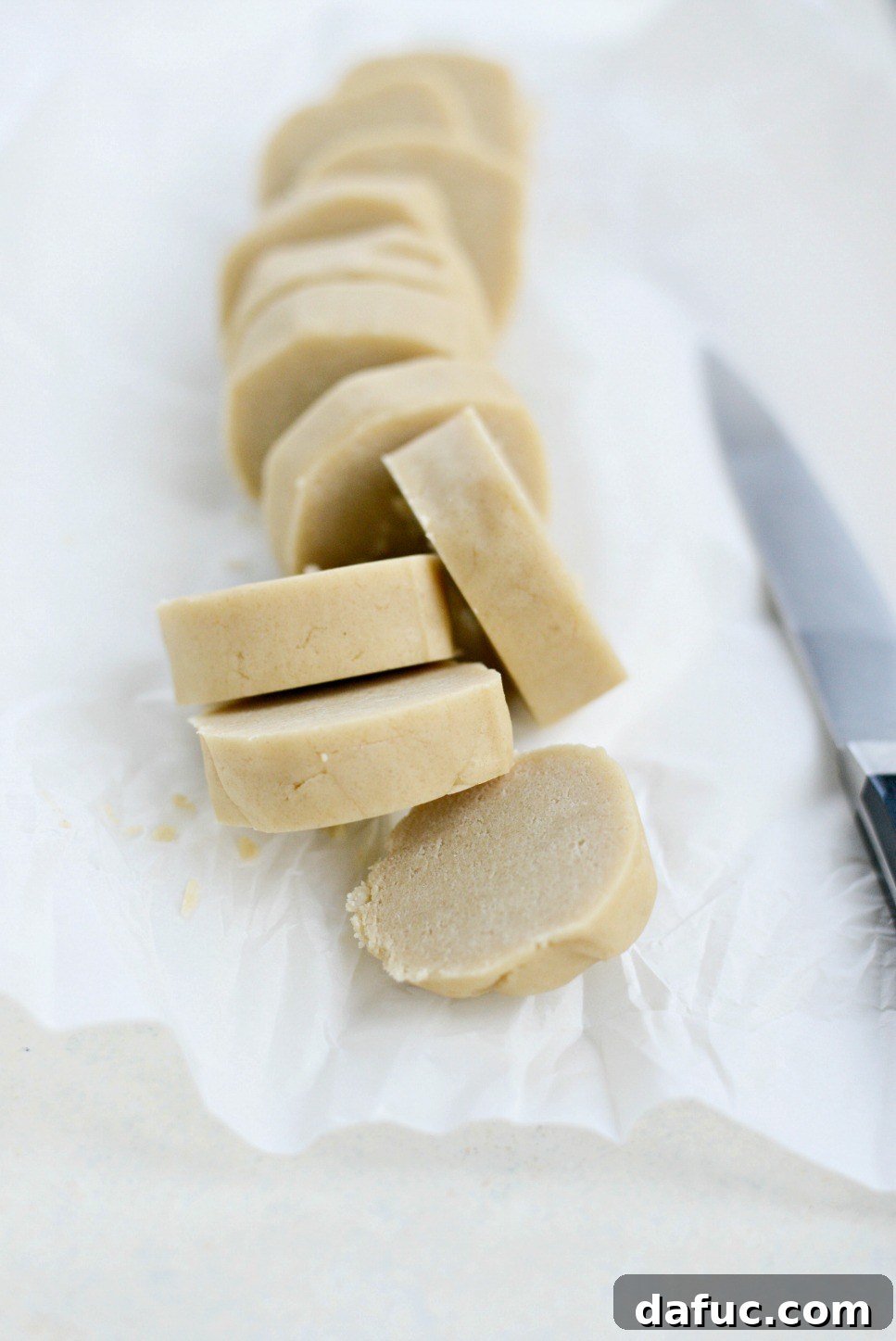 Sliced cookie dough rounds arranged on a baking sheet - Neatly sliced rounds of chilled Tahini Shortbread cookie dough are meticulously arranged on a lined baking sheet, perfectly spaced and ready to be baked to a golden crisp.