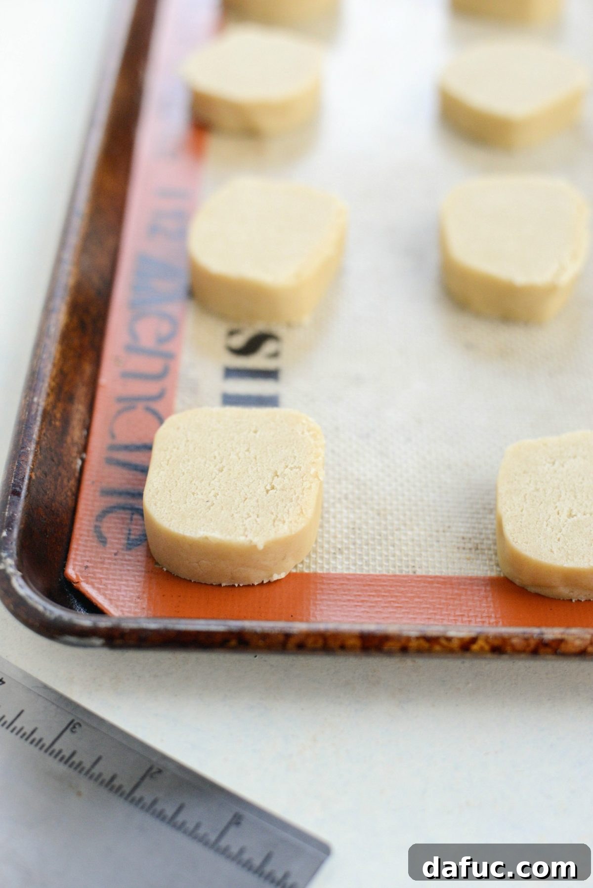 Cookie dough slices perfectly spaced on a rimmed baking sheet - The precisely sliced cookie dough rounds are neatly spaced on a silicone mat-lined baking sheet, prepared for baking and ready to transform into golden brown Tahini Shortbread Cookies.