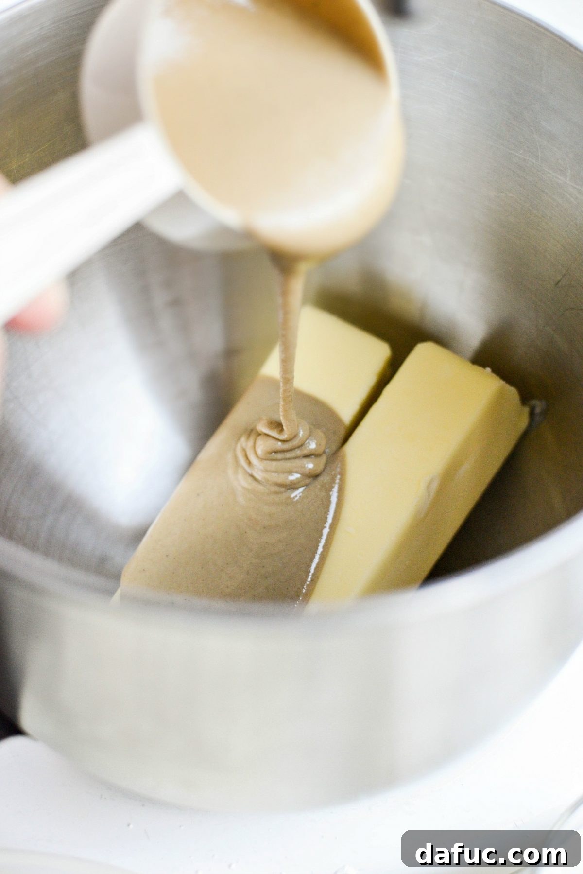 Mix butter and tahini to a light and creamy consistency in the stand mixer - The stand mixer's paddle attachment is actively mixing the butter and tahini, transforming them into a beautifully light, fluffy, and creamy consistency, indicative of proper aeration.