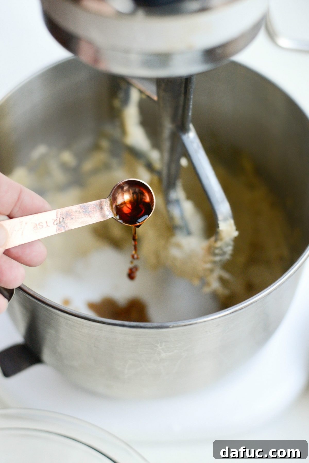 Add pure vanilla extract to the cookie dough mixture - A teaspoon of pure vanilla extract is being poured into the mixing bowl, ready to infuse the shortbread dough with its aromatic warmth.