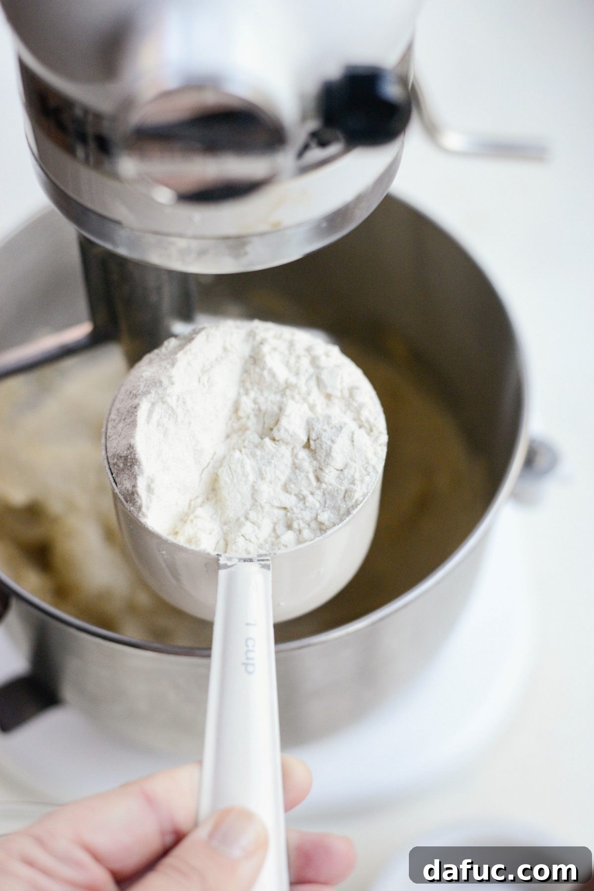 Add all-purpose flour to the wet ingredients - Unbleached all-purpose flour is being carefully added to the mixing bowl, signaling the delicate stage of combining dry and wet ingredients for the shortbread dough.