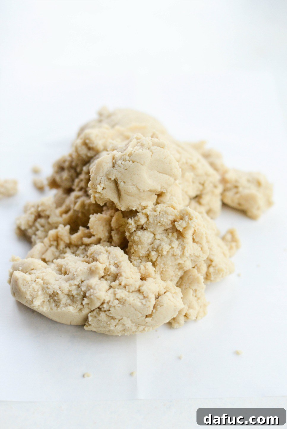 Dump out cookie dough onto parchment paper for handling - The freshly mixed Tahini Shortbread cookie dough is carefully being scooped out from the mixing bowl onto a piece of parchment paper on a clean surface, ready for shaping.