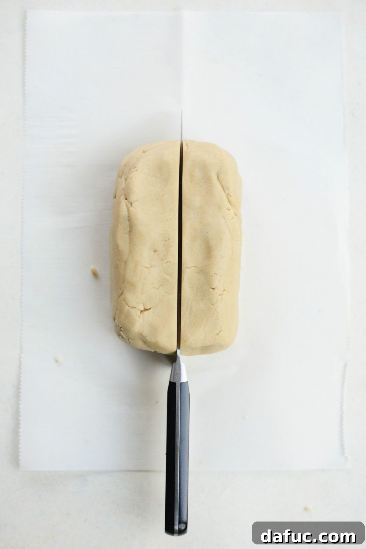 Divide cookie dough in half to form logs - The rectangle of cookie dough is being cleanly cut in half with a knife, preparing it for shaping into two uniform logs.