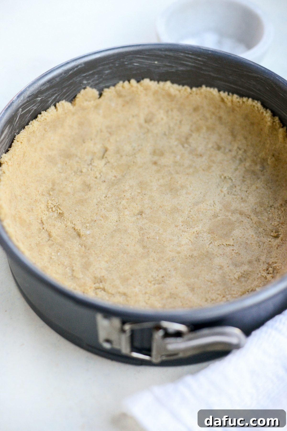 Tangy Goat Cheese Cheesecake with Tahini-Kissed Shortbread Base 6 Cheesecake crust mixture being pressed firmly into a greased 9-inch springform pan