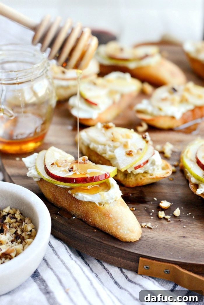 Close-up of freshly made Whipped Blue Cheese Crostini, showcasing the creamy blue cheese, thin pear slices, and honey drizzle on a rustic wooden board.