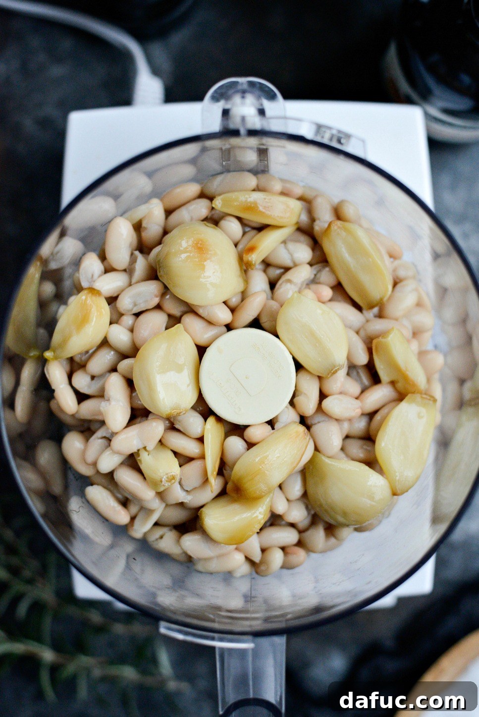 Cannellini beans and roasted garlic being added to a food processor for blending into a creamy dip.
