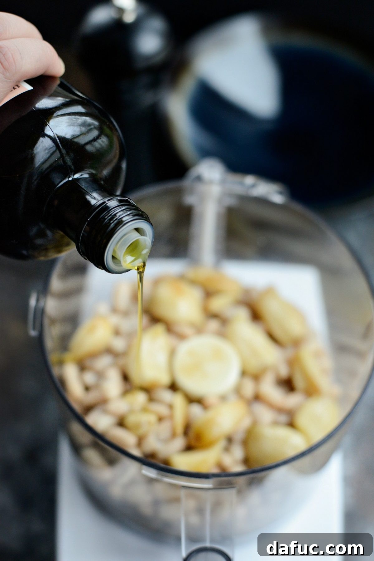 Adding broth, red wine vinegar, and olive oil to the food processor with beans and garlic.