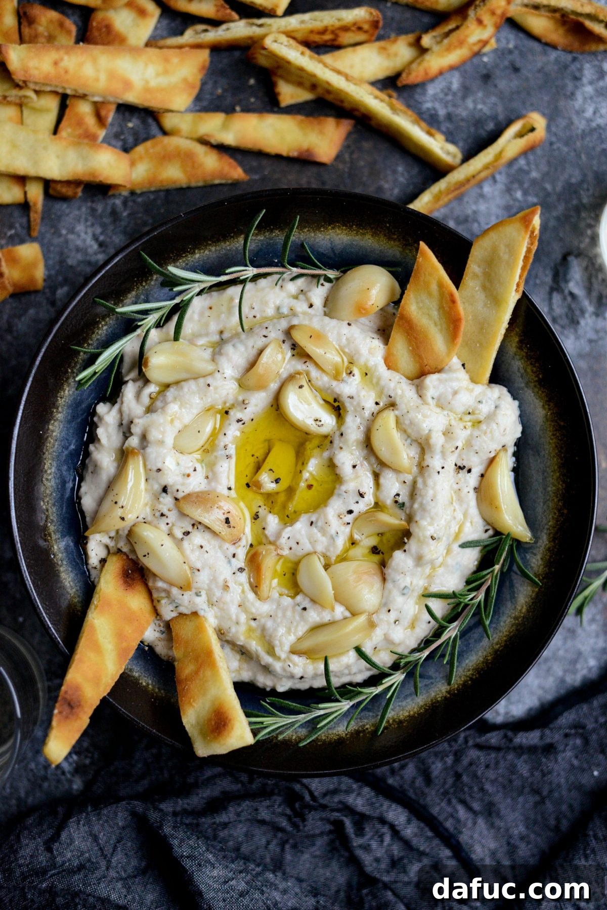 A beautifully garnished bowl of Roasted Garlic and Rosemary White Bean Dip, ready for serving.