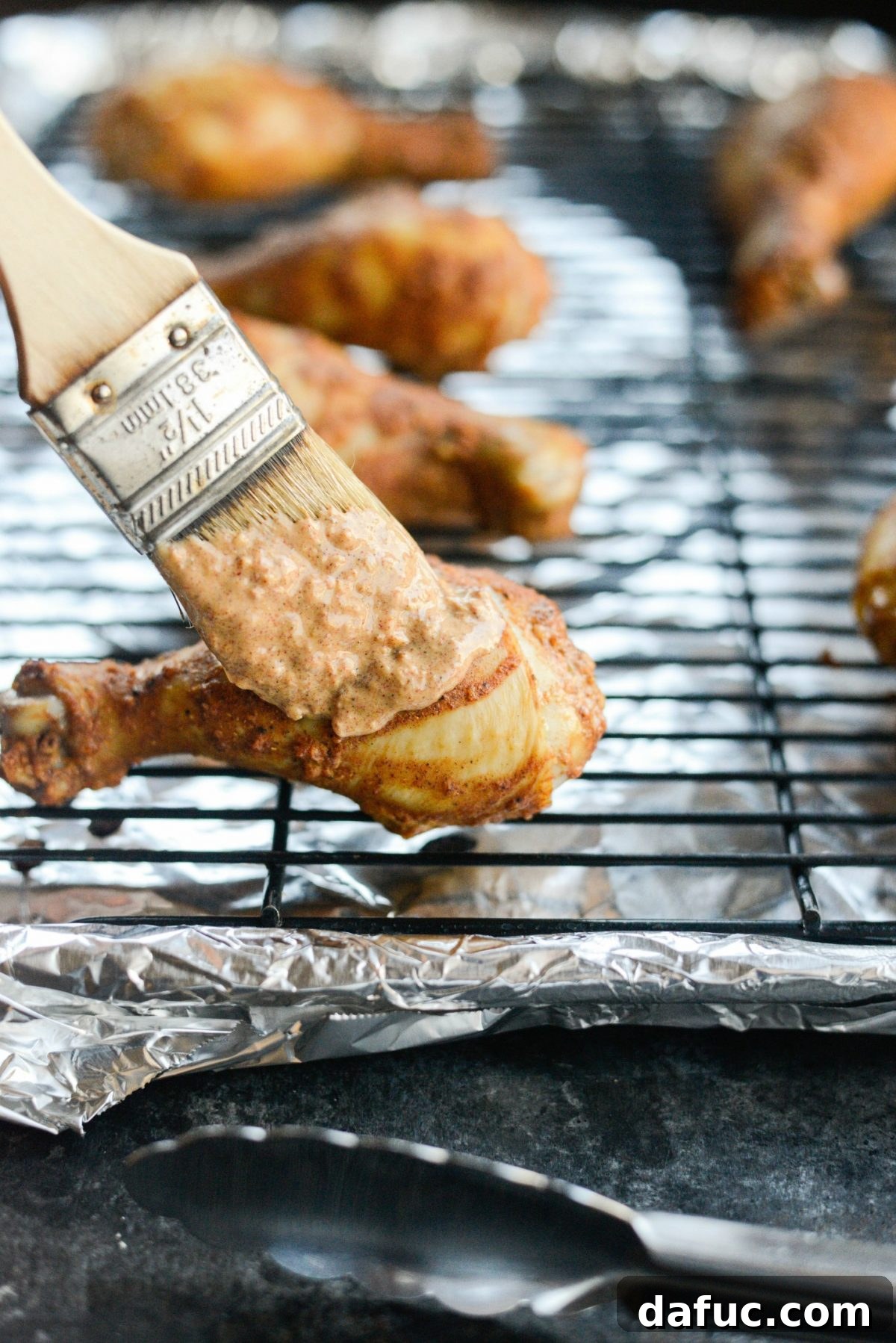 Brushing the partially baked chicken legs with the reserved tandoori marinade.