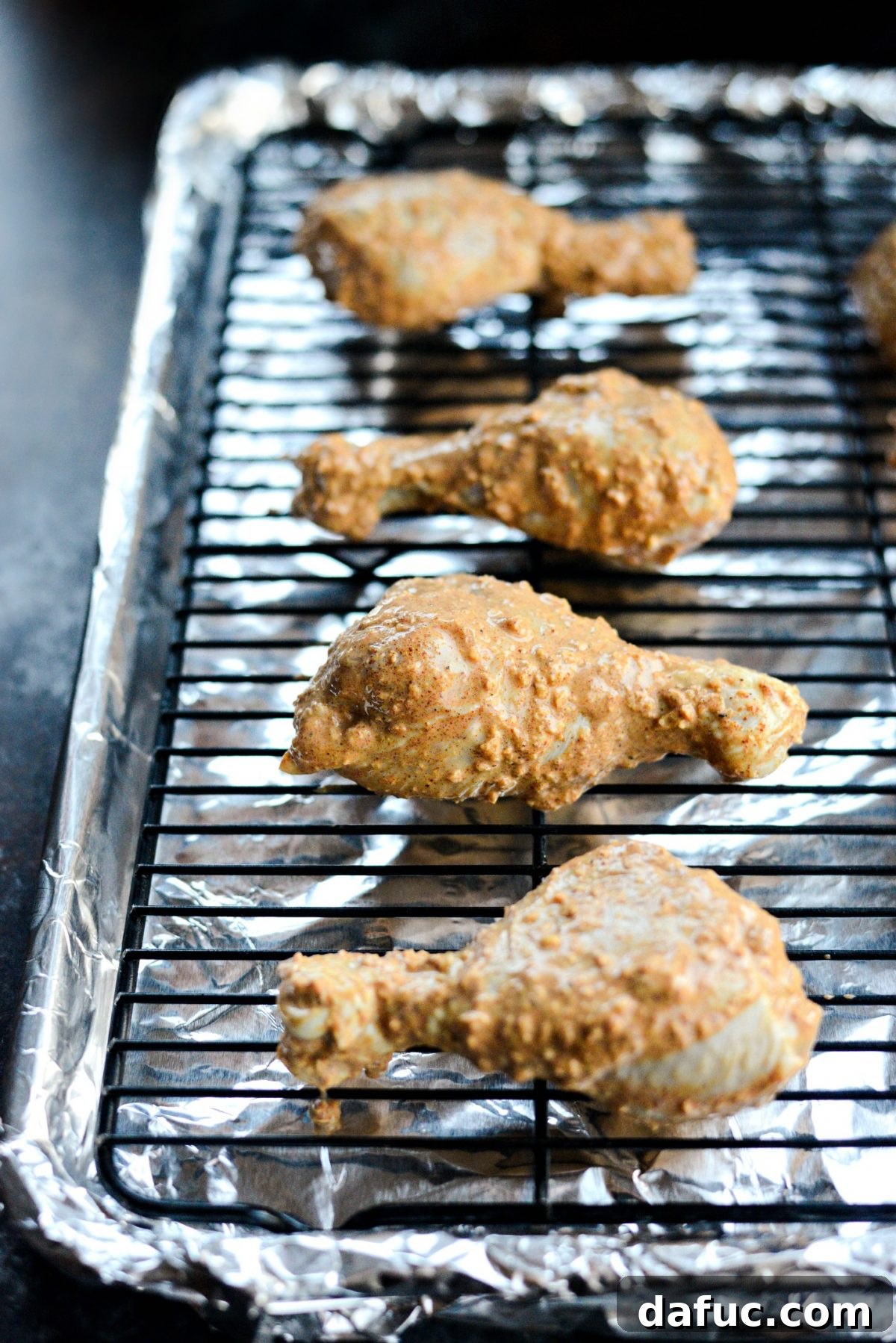 Arranging marinated chicken on a wire rack over a foil-lined baking tray before baking.
