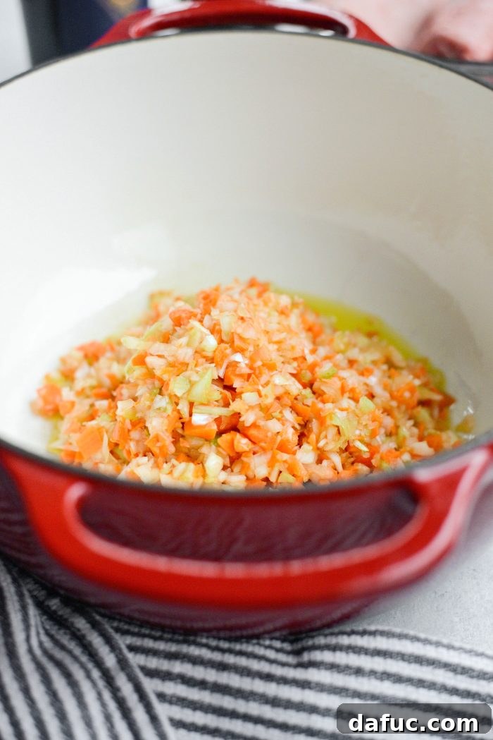 Adding olive oil and finely chopped vegetables to a large Dutch oven