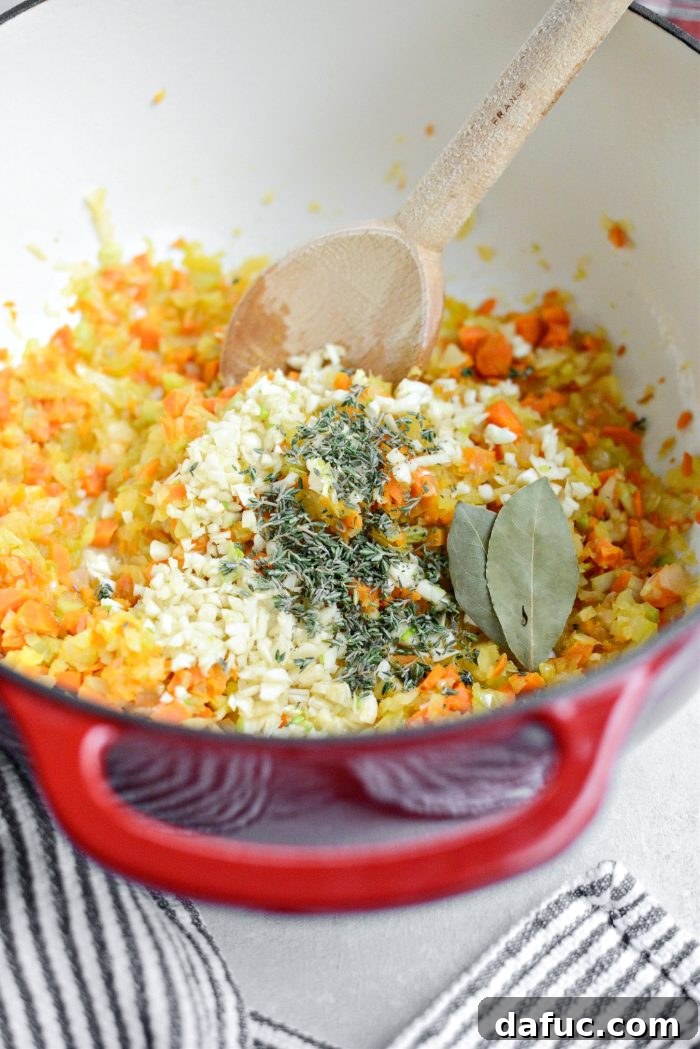 Adding minced garlic, fresh thyme, and bay leaves to softened vegetables