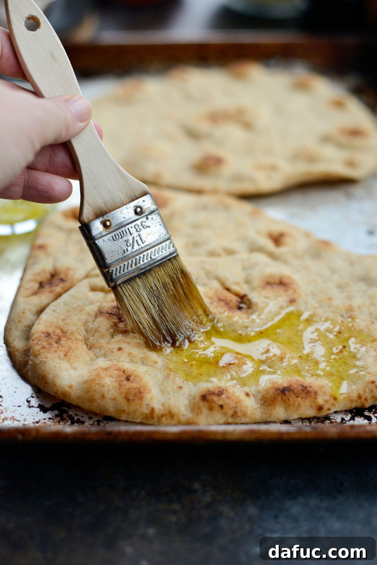 Levantine Lamb Margherita Pizza 8 A pastry brush applying garlic olive oil onto a piece of whole wheat naan, preparing it for toppings.