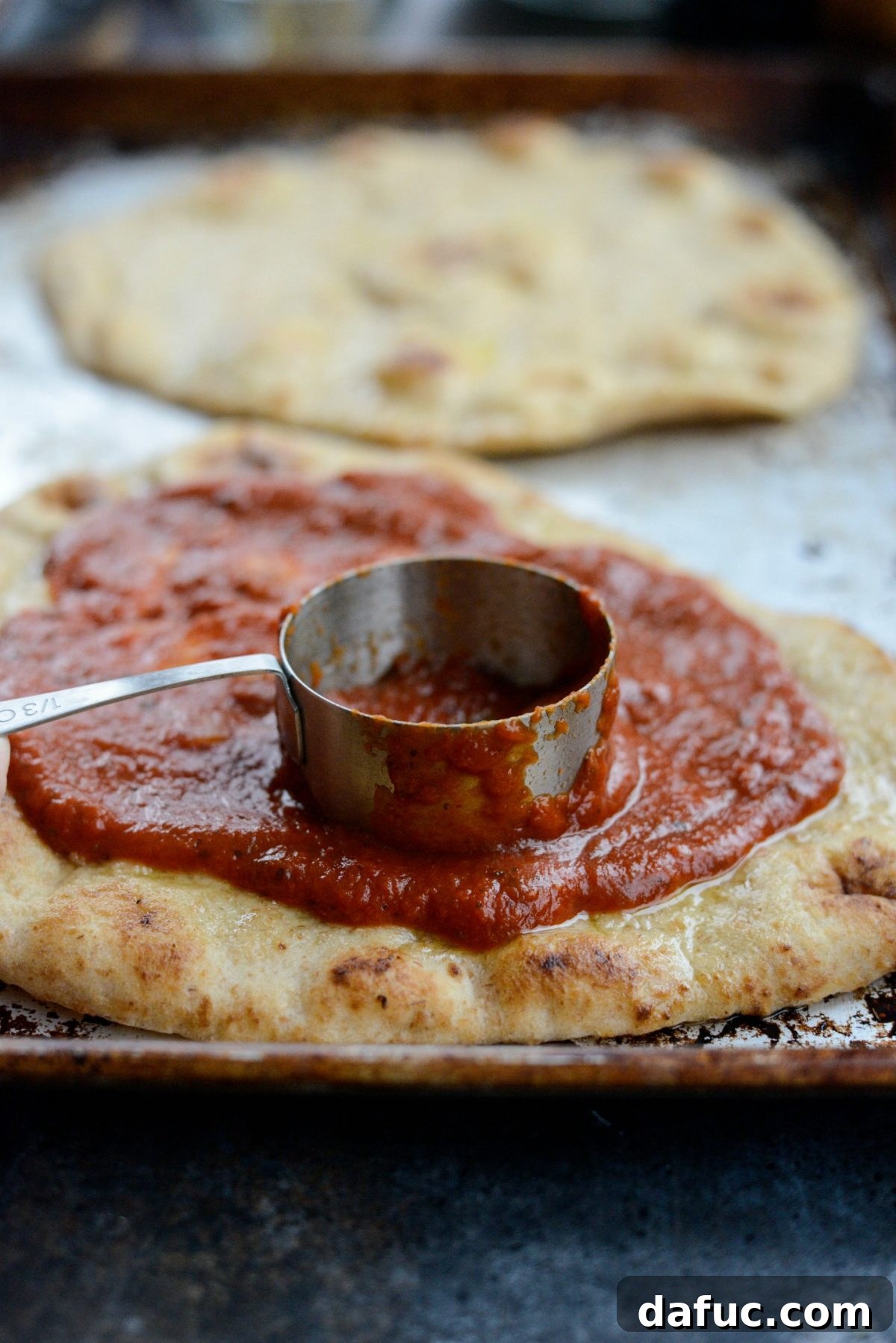 Levantine Lamb Margherita Pizza 10 Marinara sauce being spread evenly on the naan, leaving a slight border for the crust.