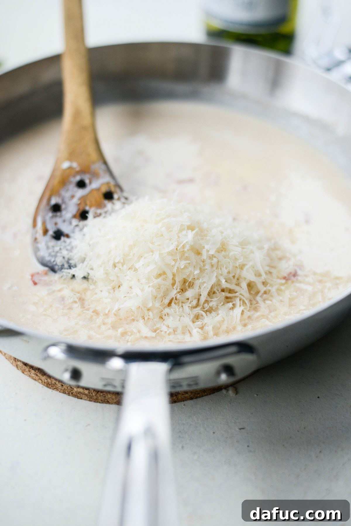 Adding freshly grated Parmesan cheese to the creamy sauce.