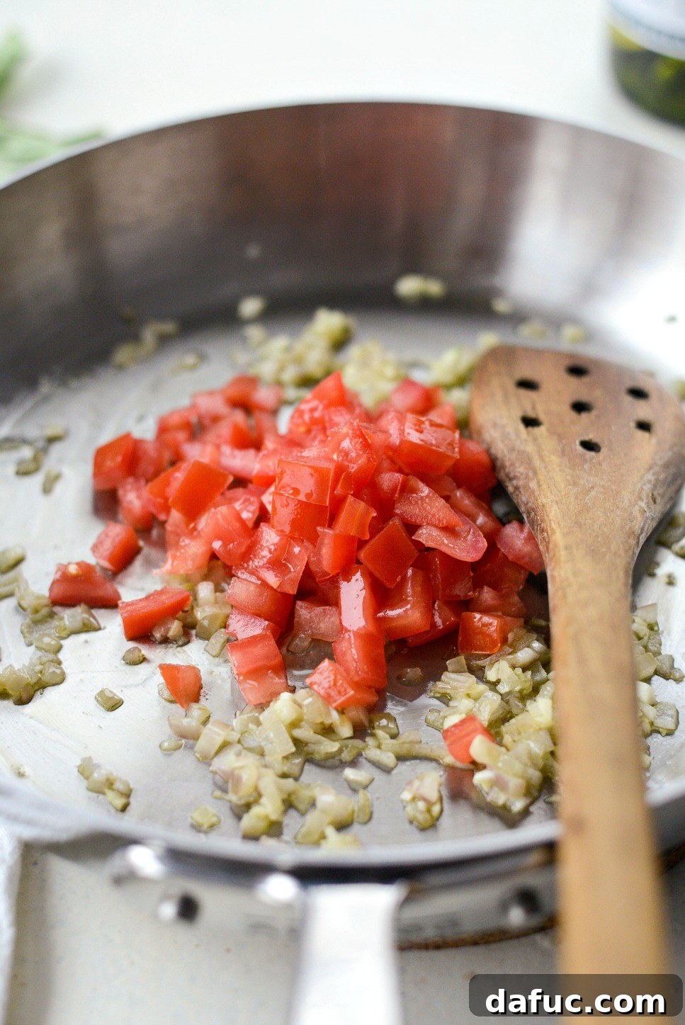 Diced Roma tomatoes being added to sautéed shallots and garlic in a pan.
