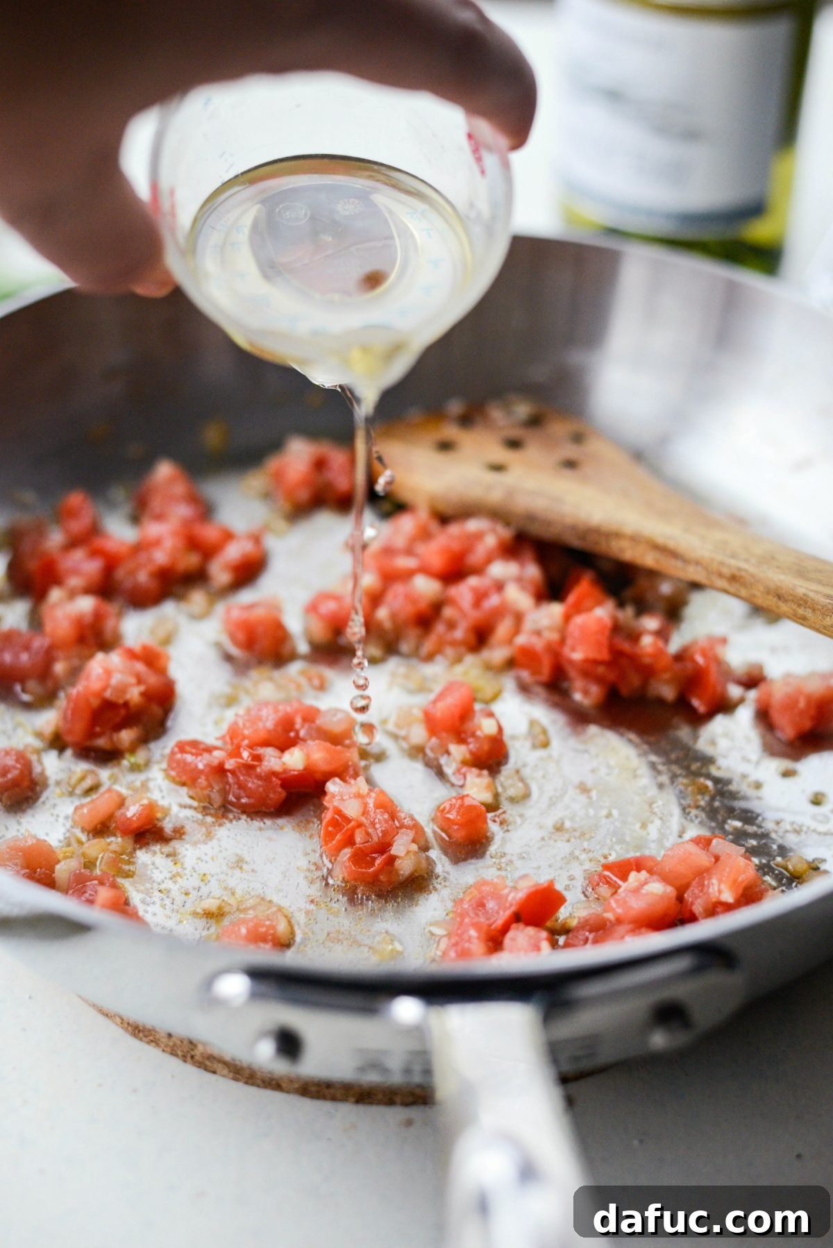Pouring dry white wine into the pan to deglaze, releasing browned bits.