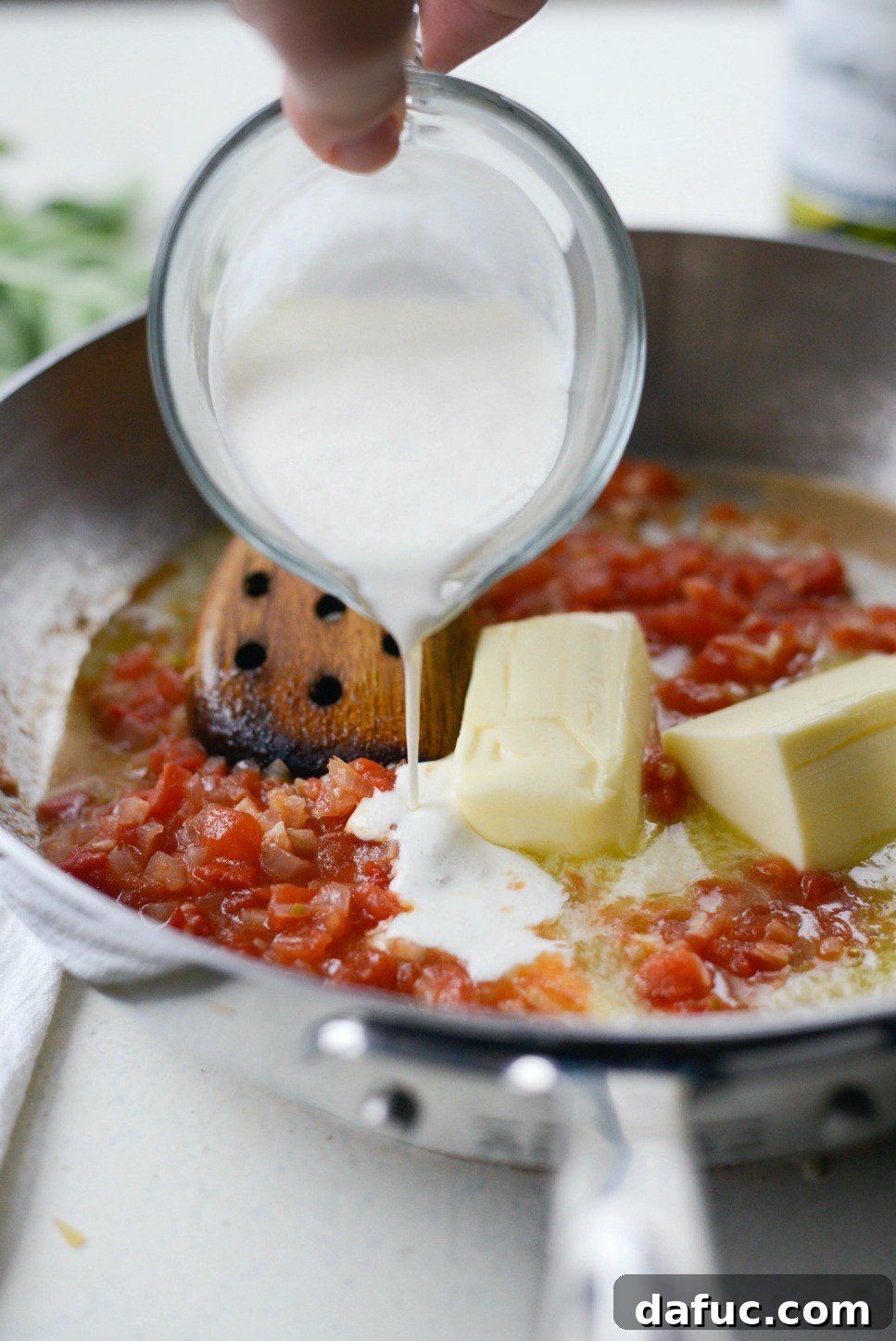 Pouring heavy cream into the sauce, creating a rich base for the fettuccine.