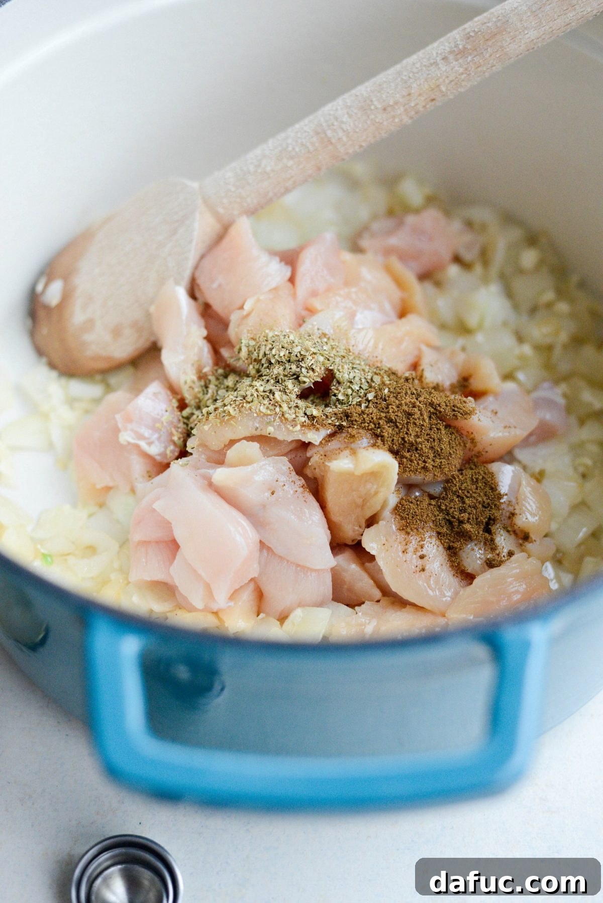 Diced chicken breast, cumin, oregano, and coriander being added to the pot.
