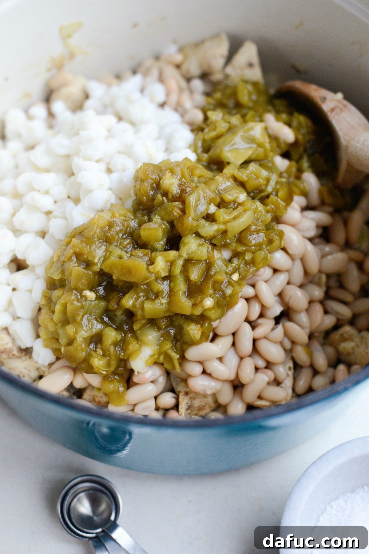 Hominy, white beans, and diced green chiles being added to the chicken and spice mixture.