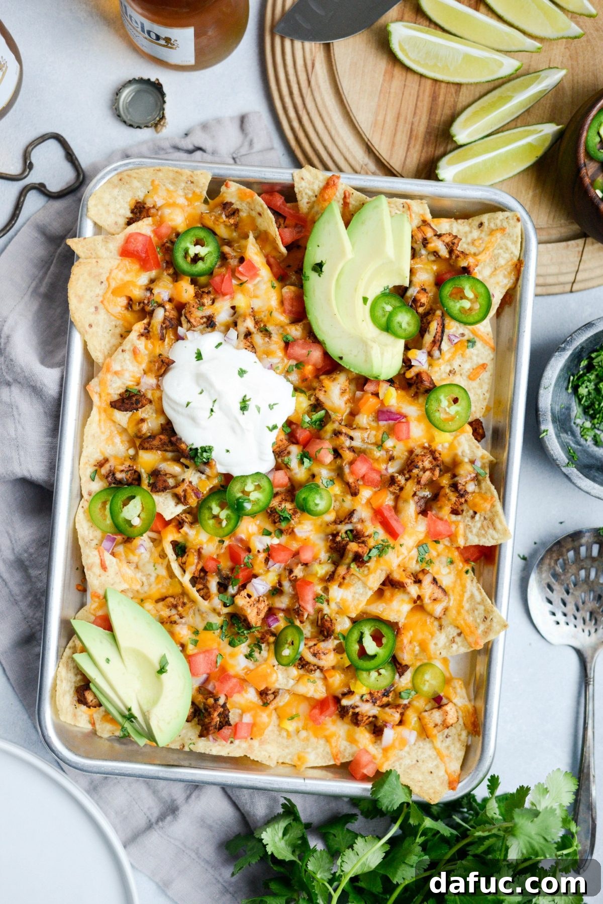Delicious Mexicali Chicken Sheet Pan Nachos spread out on a baking sheet, ready to be served, garnished with fresh cilantro and lime wedges.