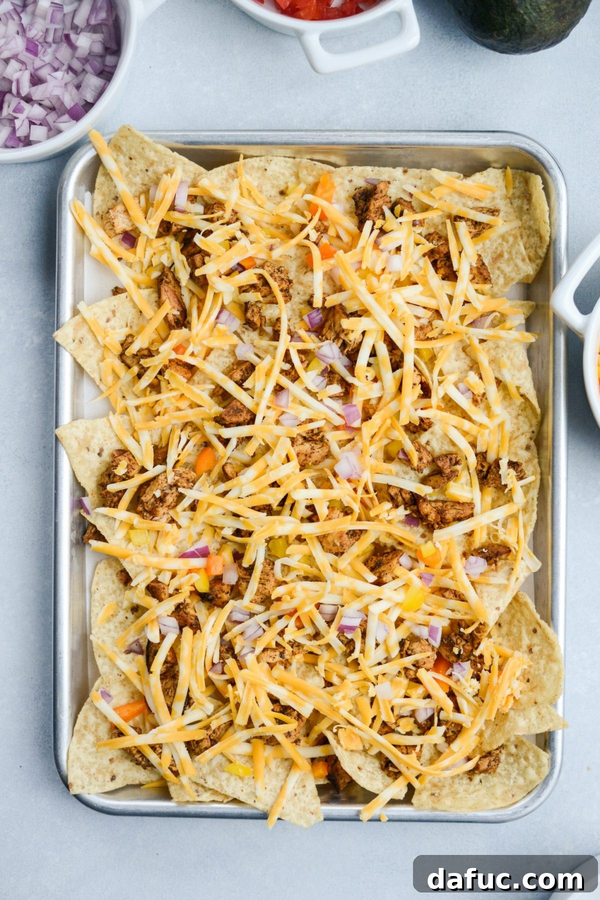 Second layer of toppings on the sheet pan nachos, including more cheese, ready for baking.