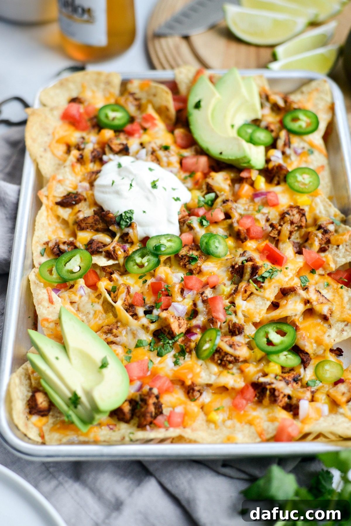 Fully dressed Mexicali Chicken Sheet Pan Nachos topped with fresh diced tomatoes, avocado slices, a dollop of sour cream, and minced cilantro.