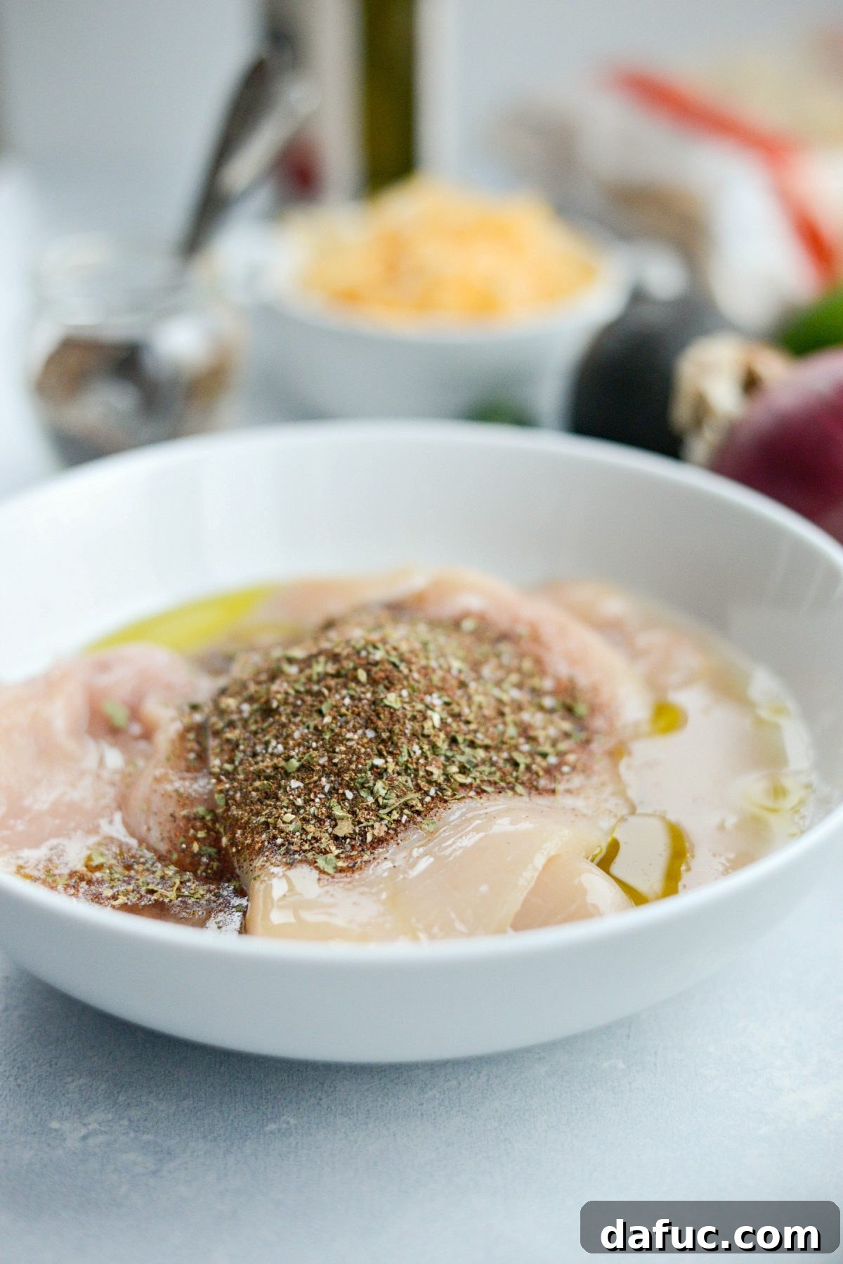 Chicken breasts in a dish with olive oil, lime juice, and Mexicali seasoning added, ready to be tossed.