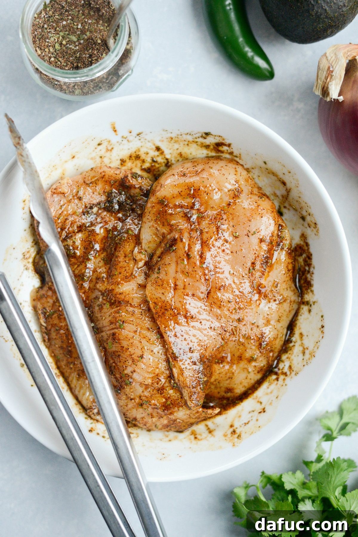 Chicken being tossed in a bowl to fully coat with olive oil, lime juice, and Mexicali seasoning.