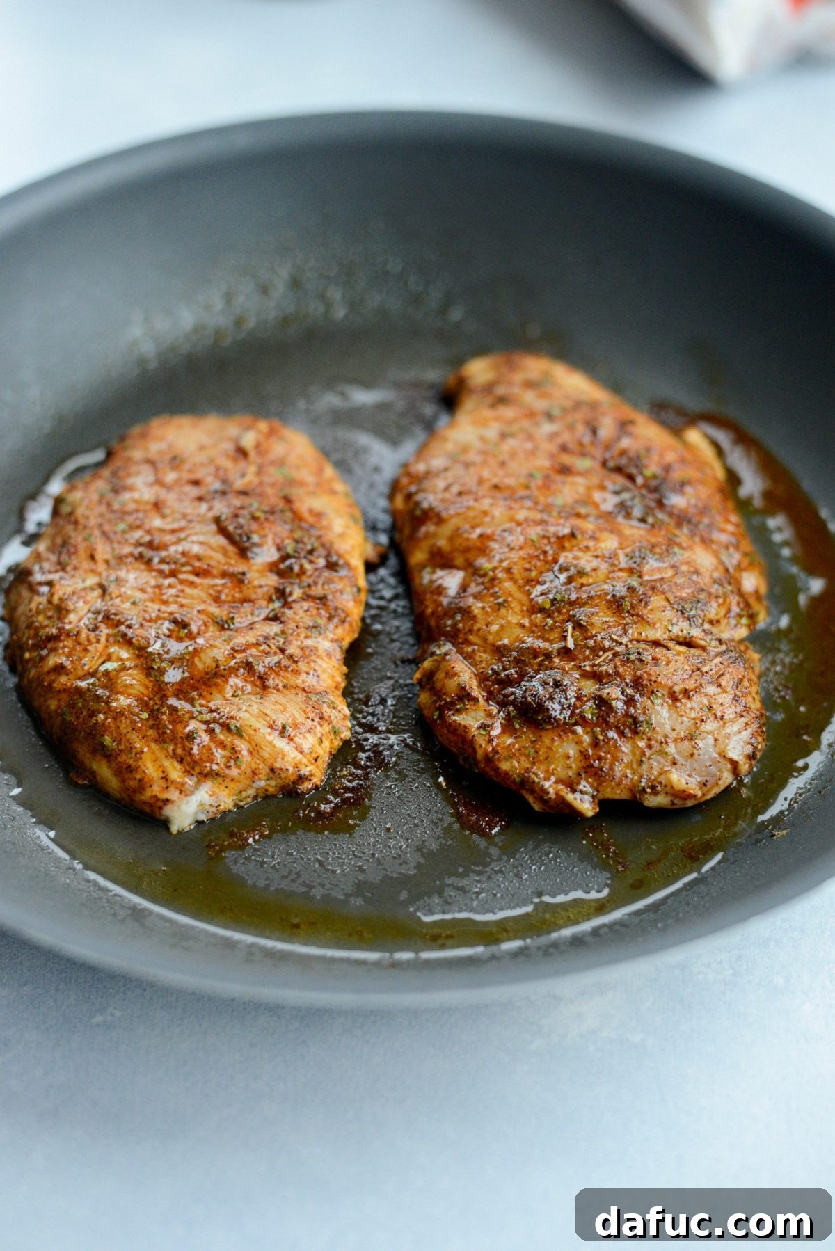 Seasoned chicken breasts cooking in a hot skillet until golden brown and cooked through.