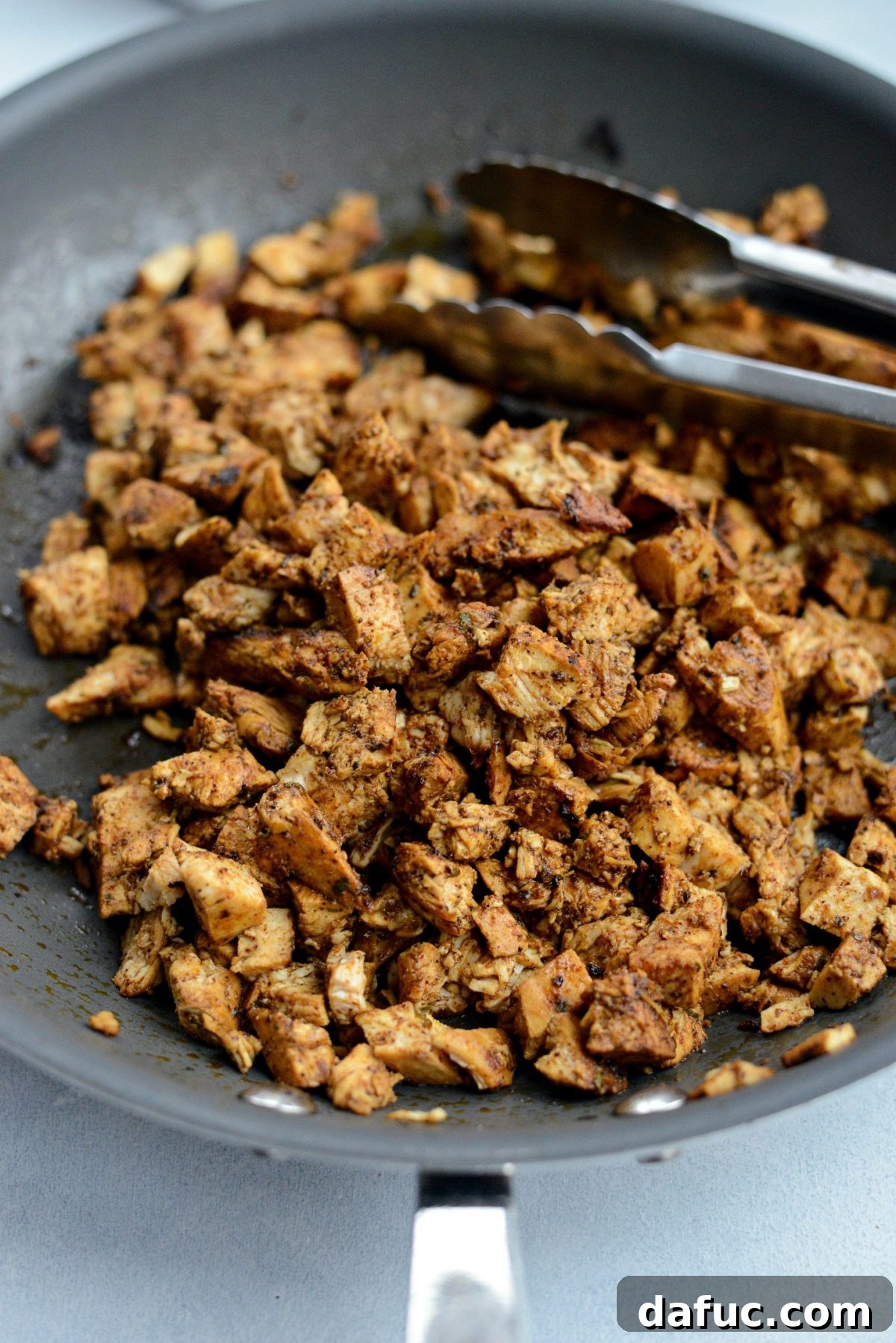 Diced cooked chicken being returned to the skillet to mix with any remaining savory bits from cooking.