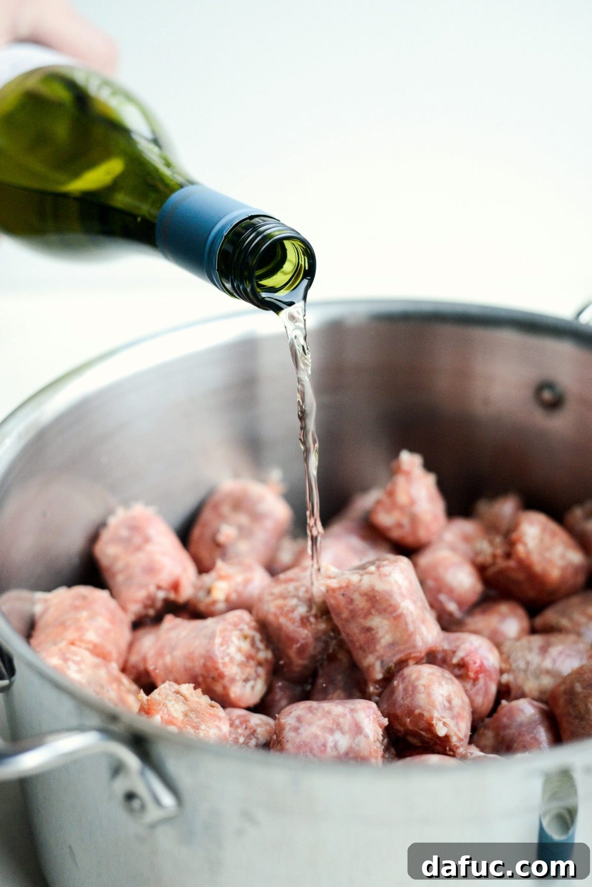 Adding sausage pieces to a pot with chardonnay