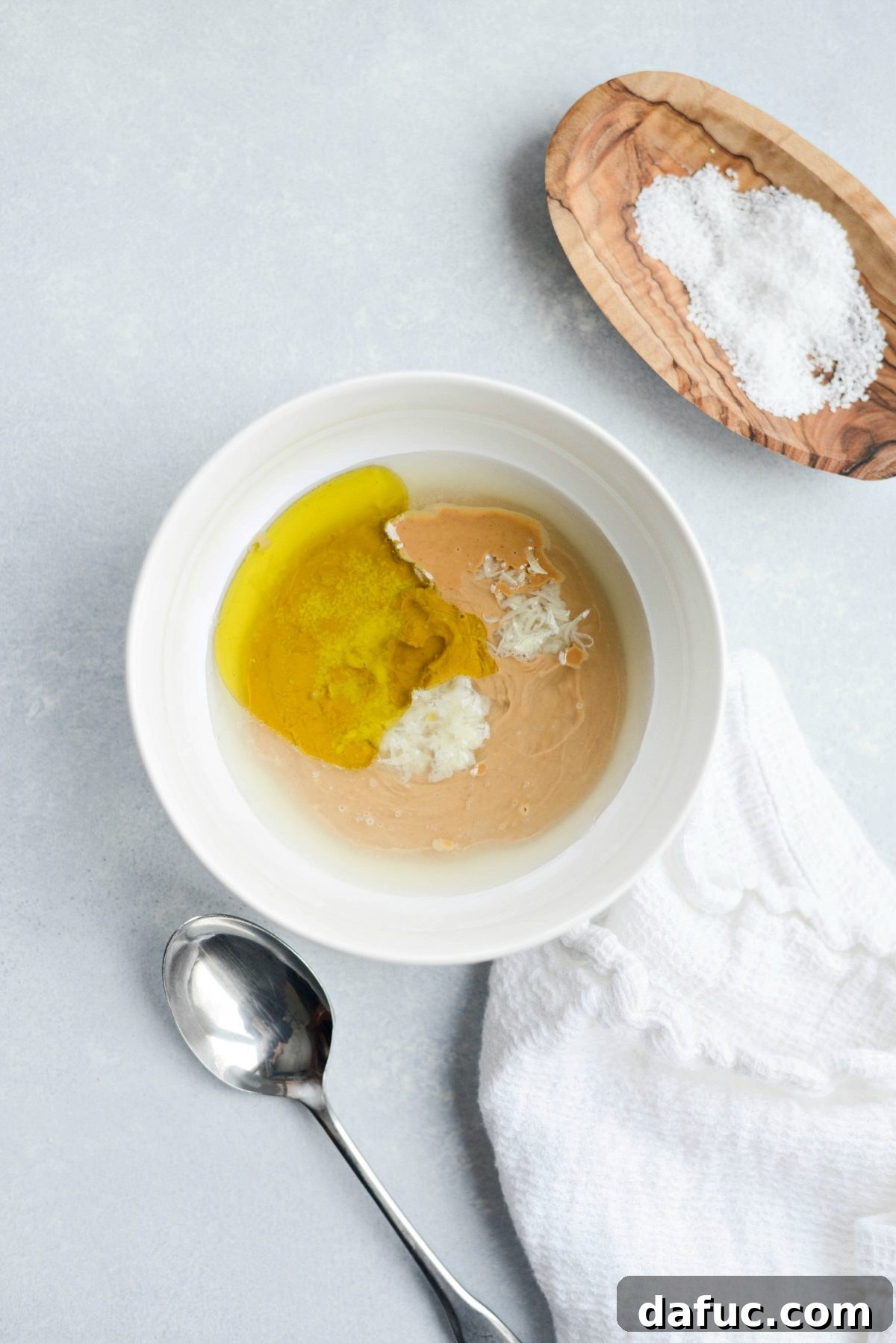 Individual ingredients for creamy cashew dressing arranged neatly in a bowl: cashew butter, lime, garlic, olive oil, salt