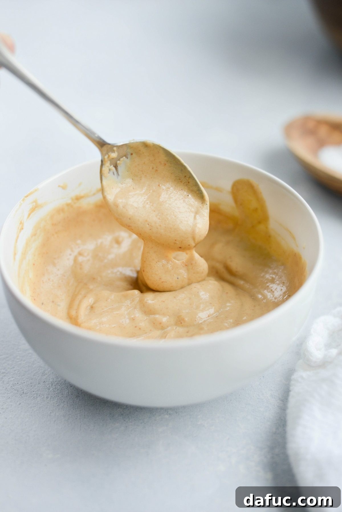 A hand stirring creamy cashew dressing in a glass bowl with a spoon