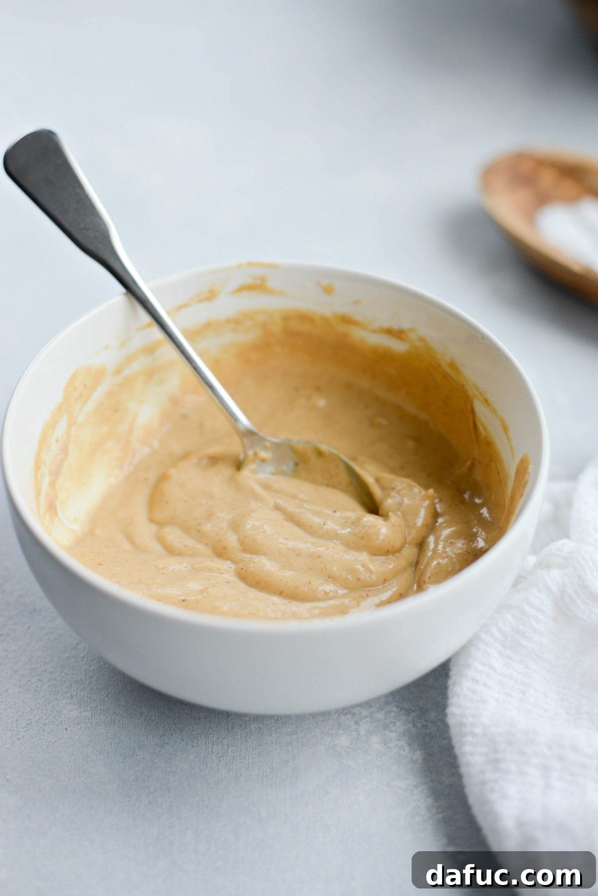 Two glass jars filled with creamy cashew dressing, placed on a wooden surface with a spoon