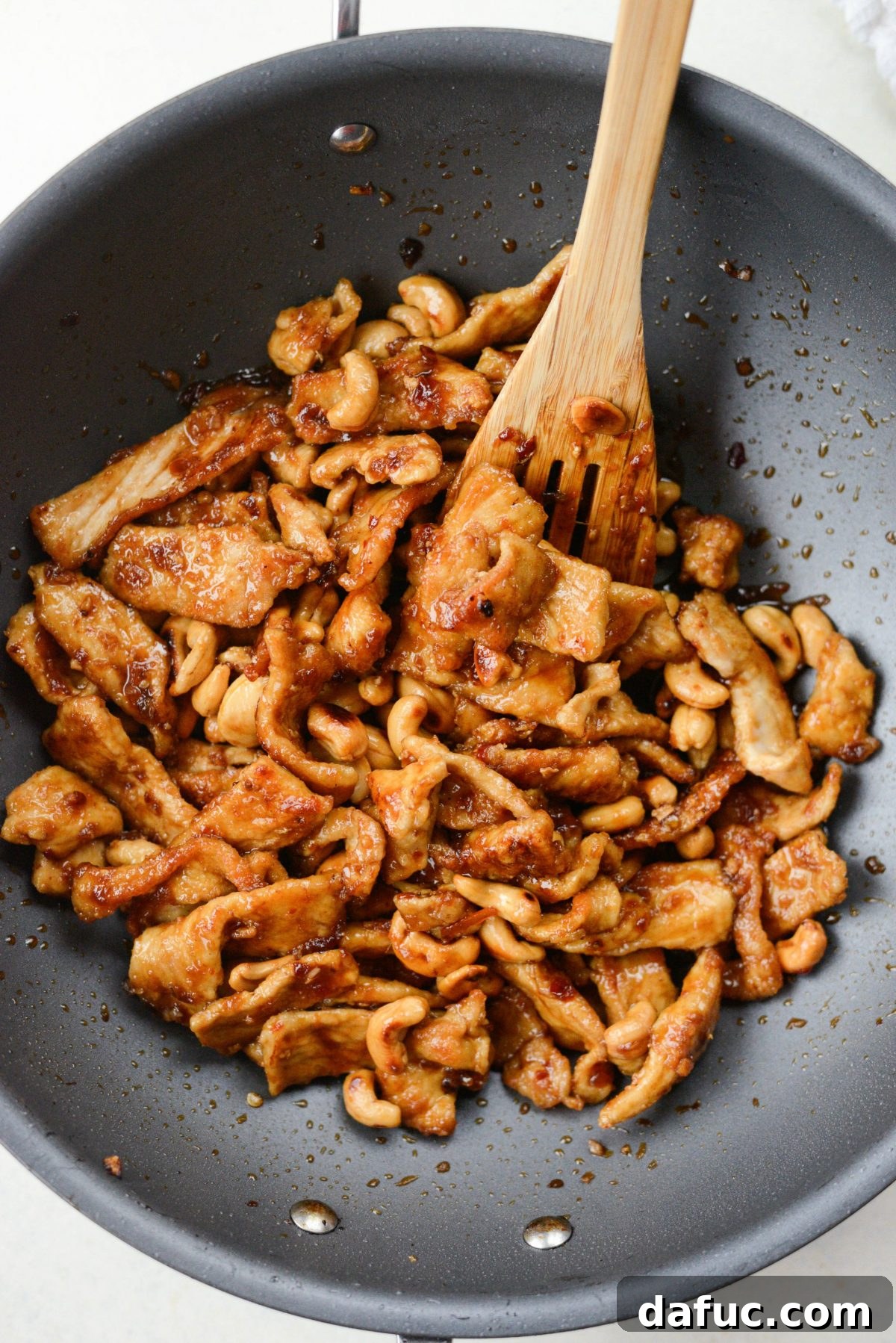 Tossing crispy pork and toasted cashews into the simmering sauce in a wok