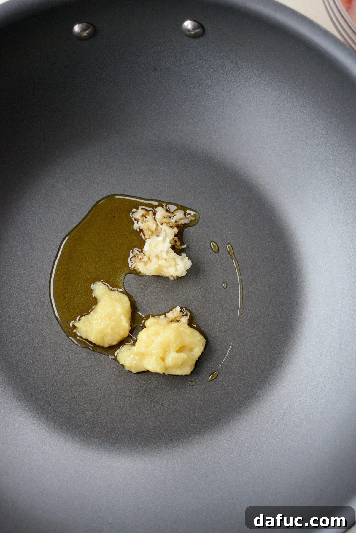 Adding sesame oil, minced ginger, and minced garlic to a hot wok or large chef's pan