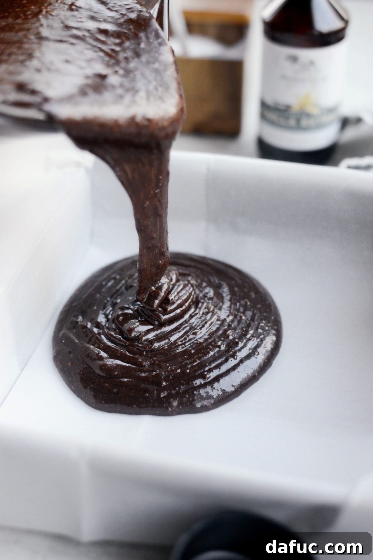 Thick chocolate Guinness brownie batter being poured into a parchment-lined 9x9 inch baking pan