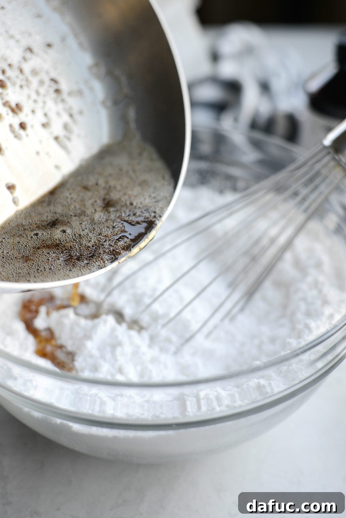 Warm browned butter being poured into a mixing bowl with sifted powdered sugar
