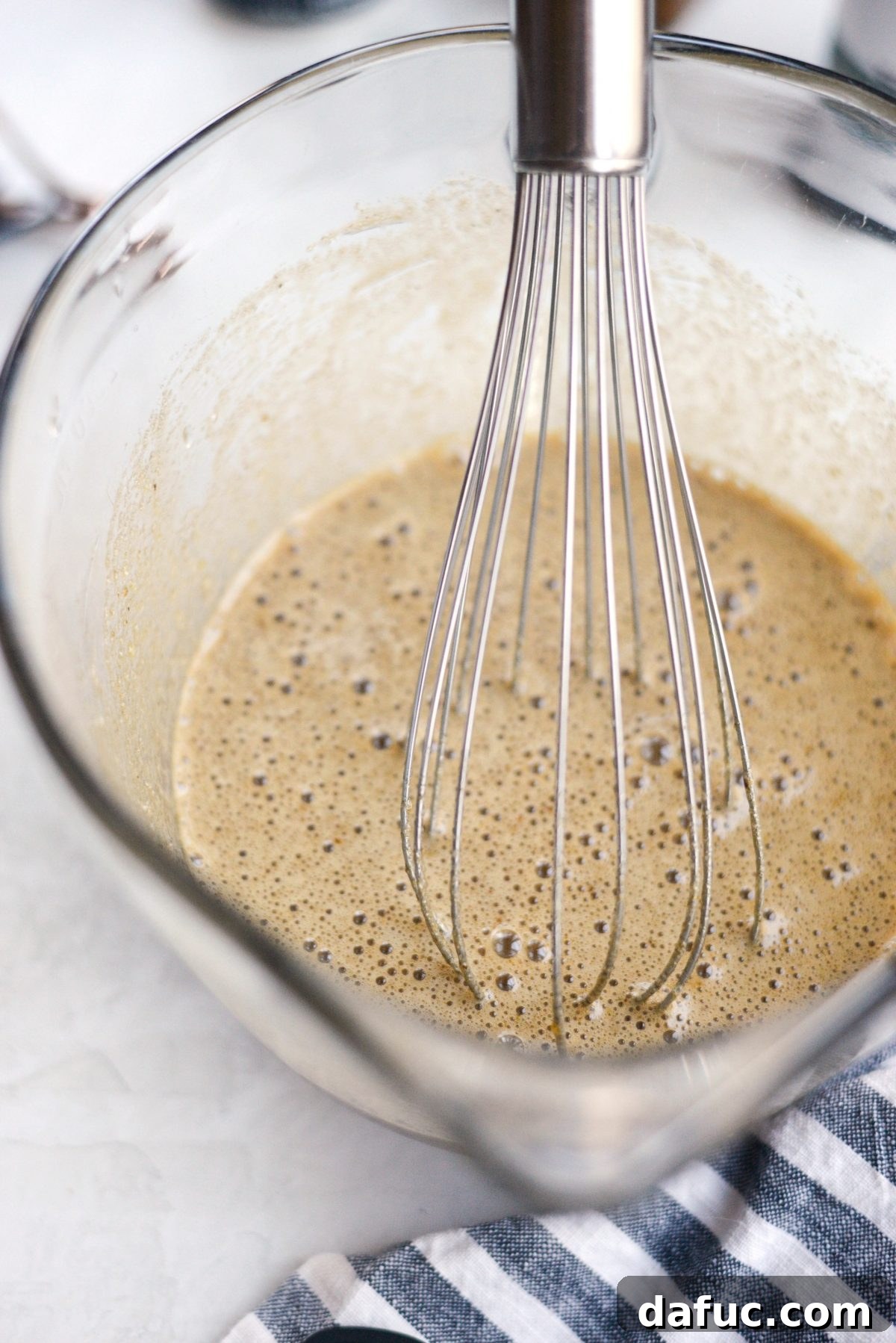 Hand whisk actively combining eggs, vanilla, sugars, and espresso powder in a mixing bowl