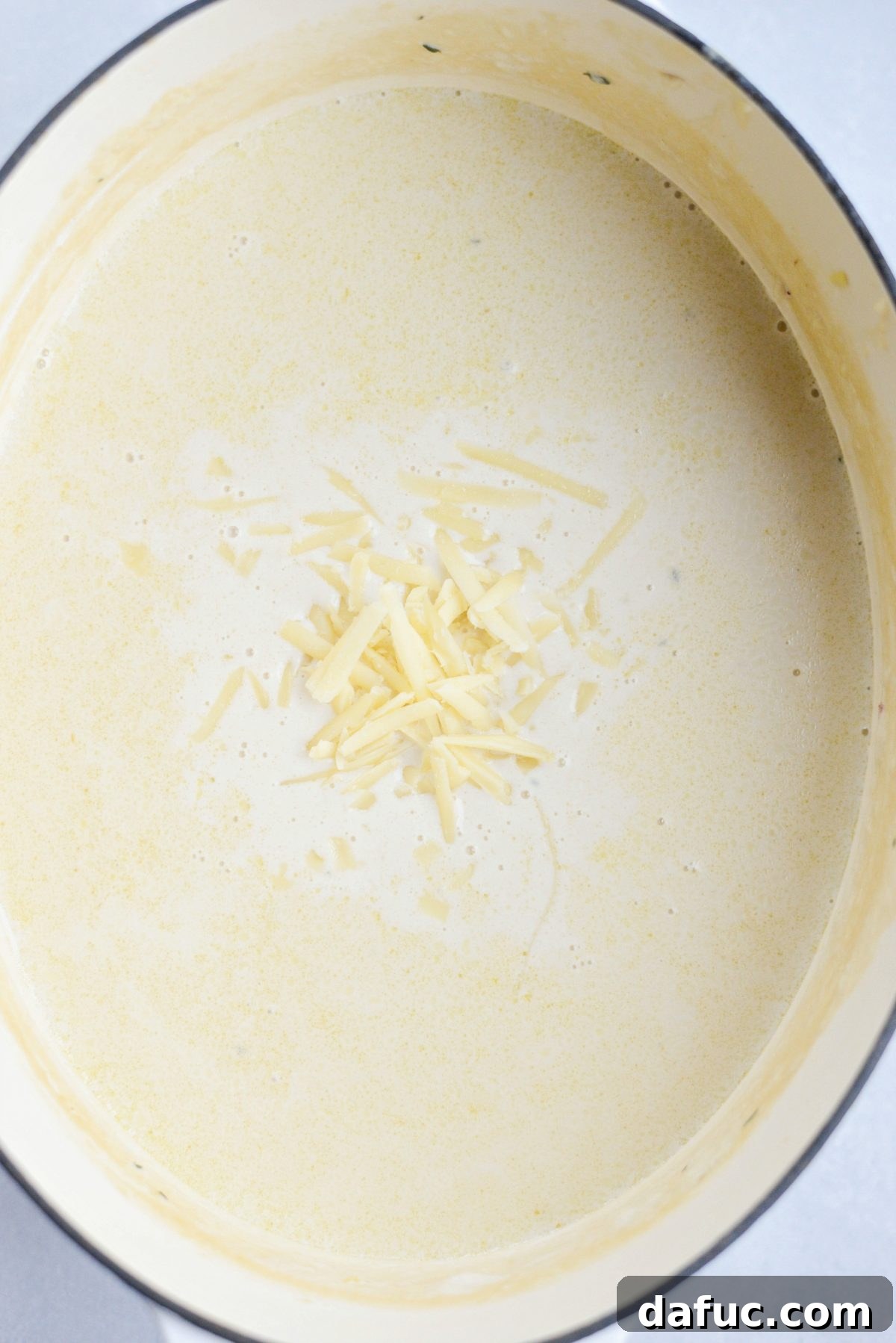 Adding freshly grated Irish white cheddar cheese to the warm, strained soup.