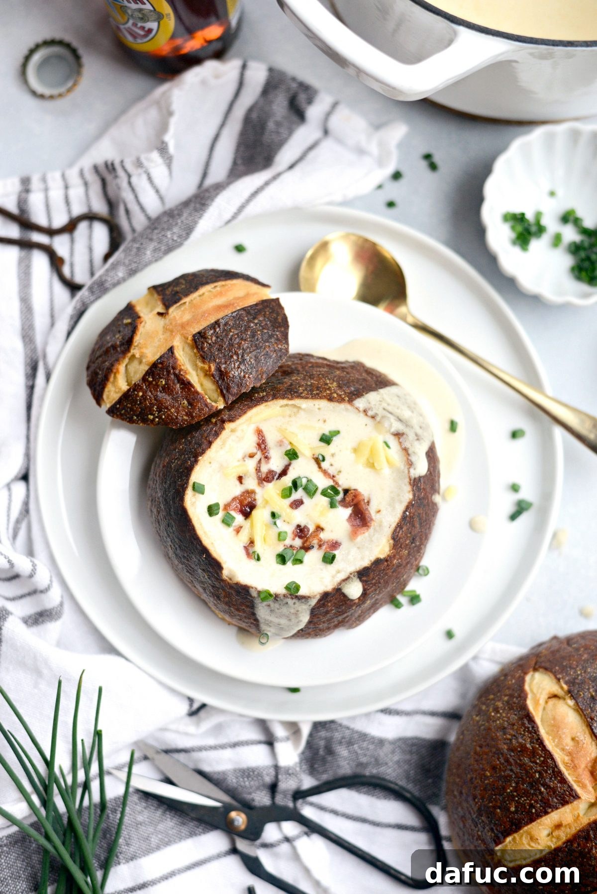 A bowl of Irish Cheddar Beer Soup in a pretzel bread bowl, generously topped with chopped bacon, chives, and shredded cheese.
