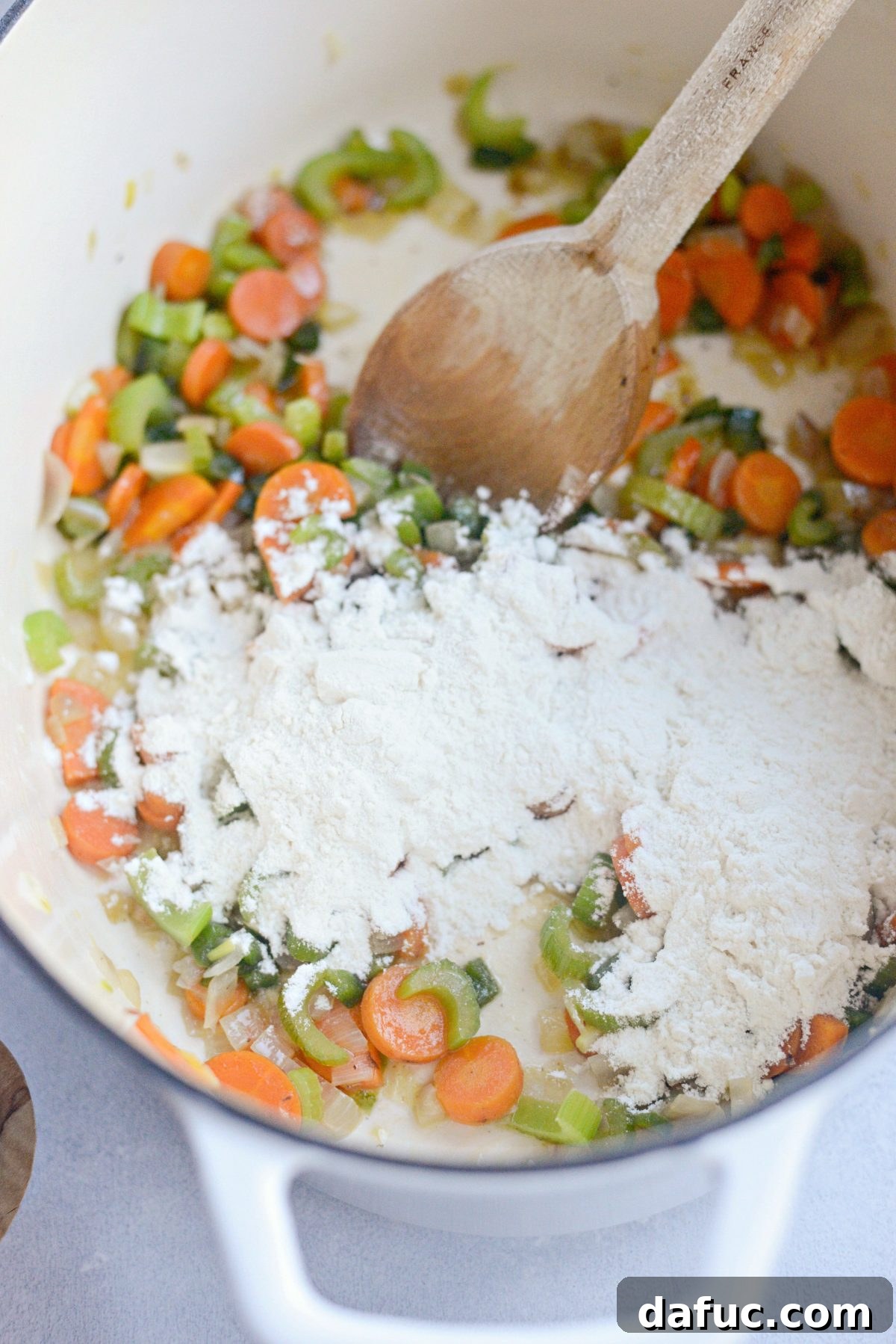 Close-up of minced garlic being added to the softened vegetables in the Dutch oven.
