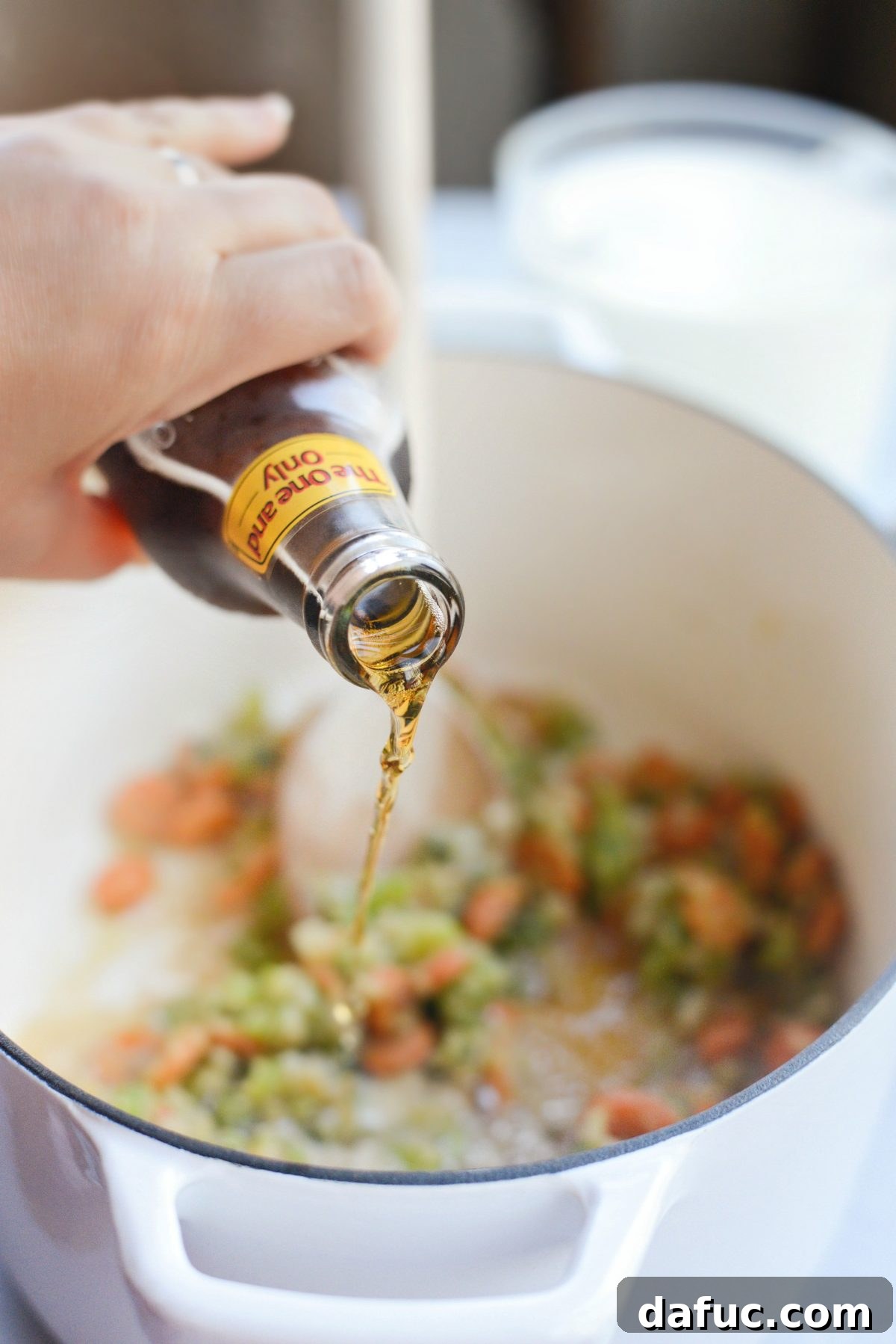 Pouring a bottle of ale into the Dutch oven with the vegetable and flour mixture, stirring to combine.